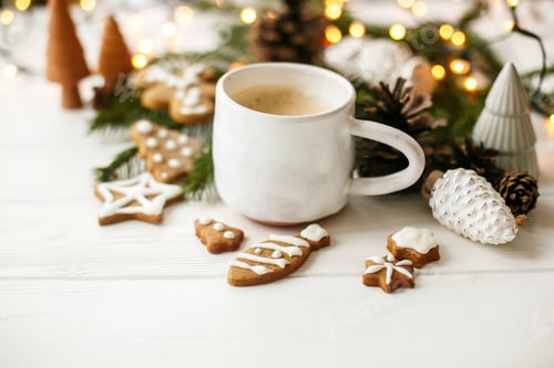 Preview: Cozy winter mood. Coffee with gingerbread cookies, pine cones and warm lights on white wooden table
