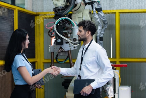 Preview: Business partner shaking hands while inspecting on industrial machine in factory