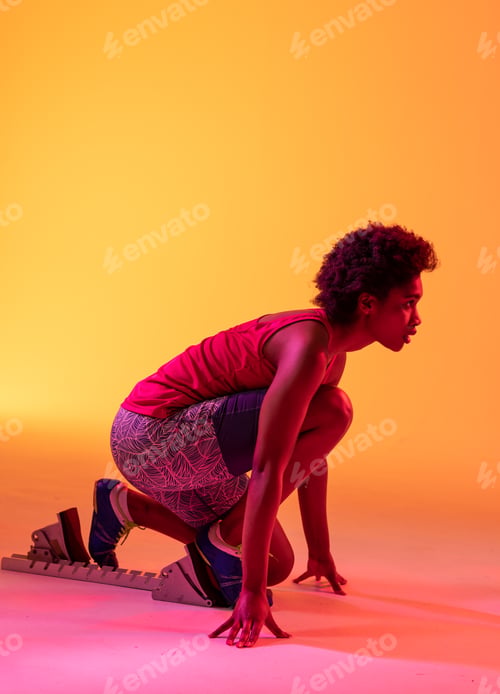 Preview: Vertical image of african american female athlete preparing for run in yellow lighting