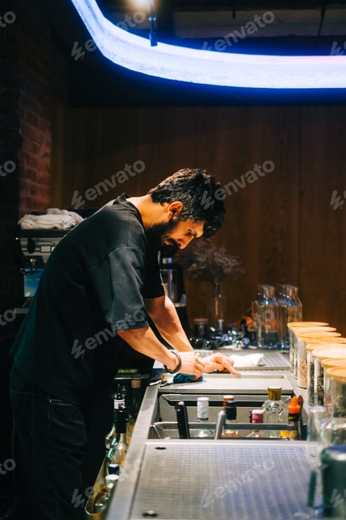 Preview: Young caucasian man asian bistro worker cleaning table on the bar counter from germs and dust.