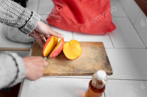 Preview: Unrecognizable young man is chopping a mango on the cutting board for breakfast.