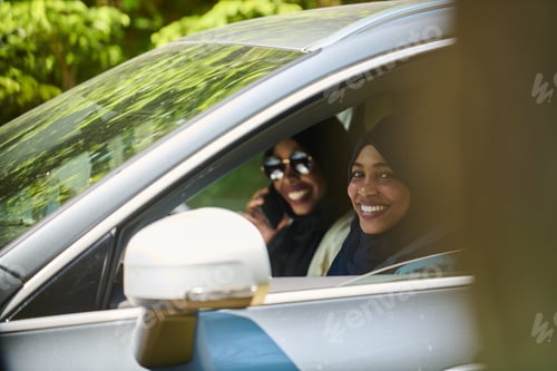 Preview: Two Muslim women wearing hijab converse on a smartphone while traveling together in a car through