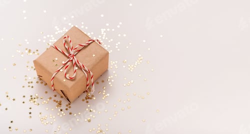 Vista previa: Caja de regalo en papel artesanal con cinta de Año Nuevo blanco-roja y estrellas de caramelo doradas sobre fondo beige