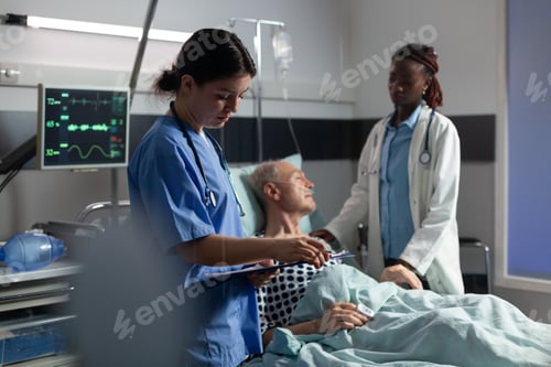 Preview: Doctor assistant taking notes on cliboard while african doctor reassuring senior patient