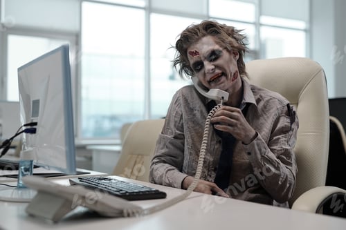 Preview: Zombie businessman with phone receiver between his shoulder and cheek looking at computer screen