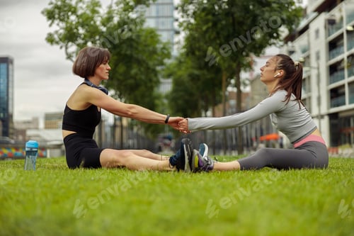 Preview: Beautiful young women doing stretching exercise on green grass at city park
