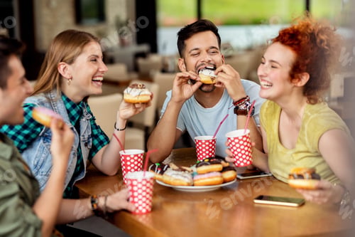 Preview: Group of cheerful friends eating donuts in a cafe.