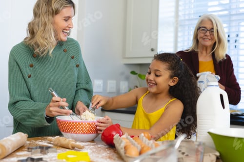 Preview: Multiracial senior woman looking at happy daughter and granddaughter mixing food in bowl in kitchen