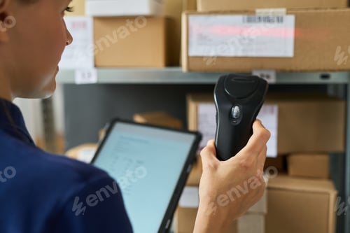 Preview: Young Adult Caucasian Woman Scanning Packages with Barcode Reader in Warehouse