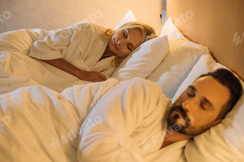 Preview: beautiful mature couple in bathrobes sleeping together in bed in hotel room