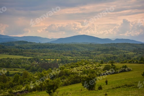 Preview: Aerial view of a lush, green grassy field with hills under a cloudy sky