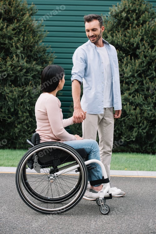 Preview: happy man holding hands with disabled girlfriend while walking in park together