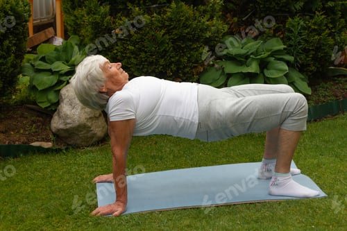 Preview: age-old gray-haired woman does therapeutic exercises for the muscles of the press and back, spine