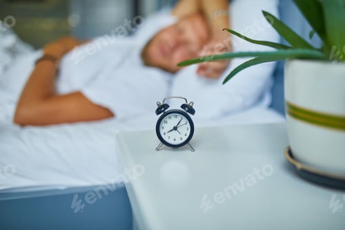 Preview: Bearded man is sleeping alone on a big and cozy bed white linens with alarm clock