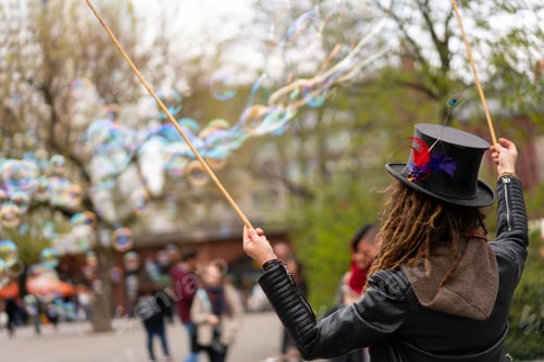 Preview: Closeup shot of a person with a funny hat blowing bubbles with two sticks in the park