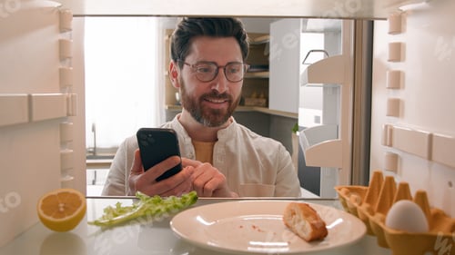 Preview: Man hungry guy open empty refrigerator with half lemon, nasty lettuce leaf, one egg, slice of bread