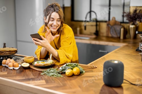 Preview: Woman speaking to a smart speaker during a breakfast at home