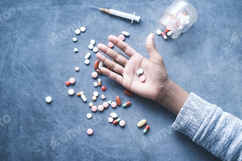 Preview: drug addiction concept with hand holding pills and syringe laying on floor
