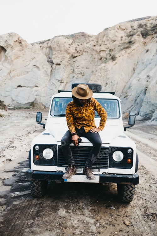Preview: Stylish man sitting on car in canyon