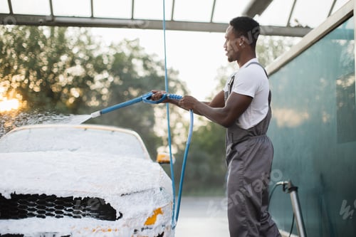 Preview: African man washing his yellow car with foam at self service carwash outdoors.