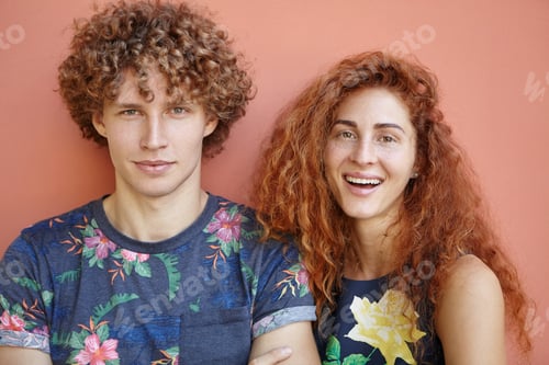 Preview: Convienced curly guy wearing T-shirt with flower coloring standing near his girlfriend with bushy re