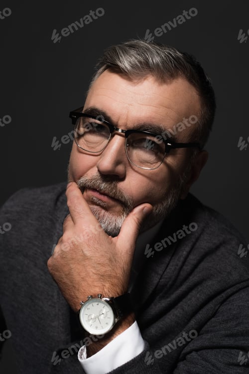 Preview: portrait of serious senior man in eyeglasses and wristwatch looking at camera isolated on dark grey