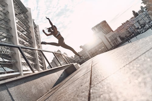 Preview: Long jump. Full length of modern young woman in sports clothing jumping while exercising outdoors