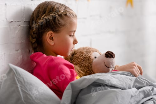 Preview: Side view of cute child lying in bed with teddy bear