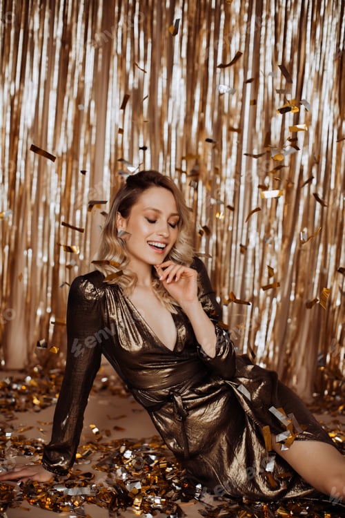 Preview: Attractive lady in elegant dress coquettishly smiles and touches her chin while sitting on gold bac