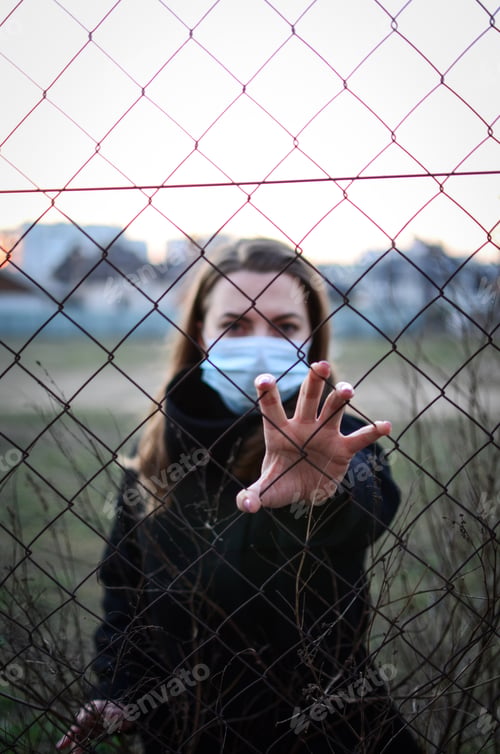 Preview: Girl in a protective mask pulls his hand to the fence. Closed borders of countries. Cov pandemic.