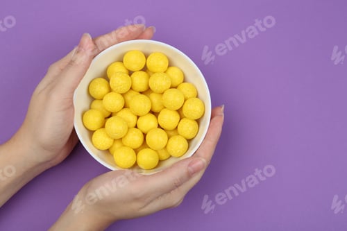 Vista previa: Woman holding bowl of lemon drops on purple background, top view