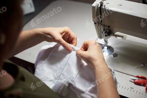 Preview: Needlewoman draping white garment with needle and her hands.