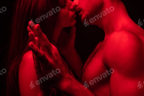 Preview: side view of passionate undressed sexy young couple kissing and holding hands in red light isolated