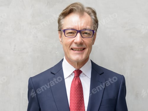 Preview: Face of happy handsome mature businessman with eyeglasses smiling against concrete wall