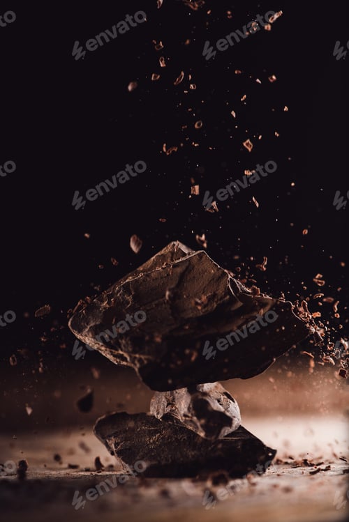 Preview: close up image of grated chocolate falling on pieces of chocolate on black background