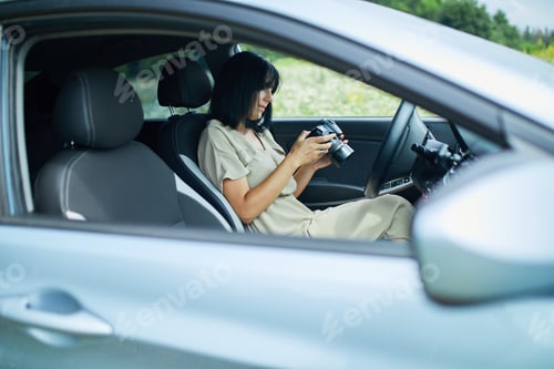 Preview: Woman photographer sitting in the car and looking on the photo on the camera