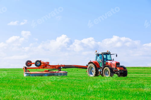 Preview: A rotary mower attached to a tractor moves in the field and mows fresh green grass for silage.