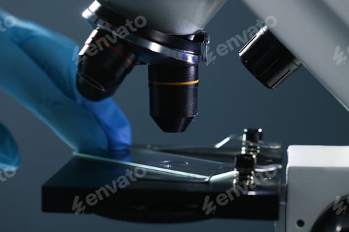 Preview: Scientist working with microscope on dark background, closeup