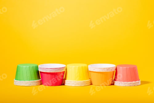 Preview: Multi-colored paper molds for muffins and cupcakes on a yellow background copy space