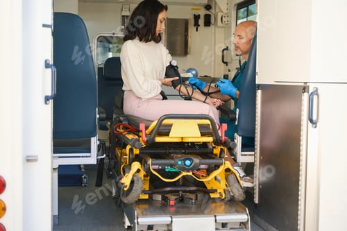 Preview: Woman sits in an ambulance with blood pressure monitor on arm