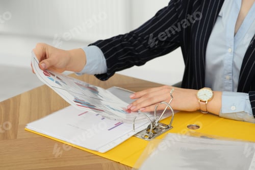 Preview: Businesswoman putting document into file folder at wooden table in office, closeup