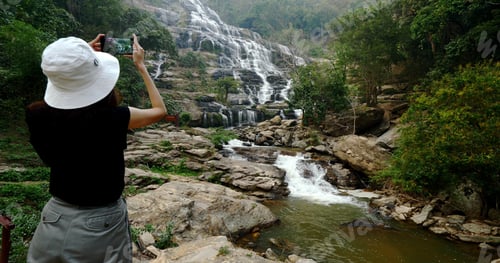 Preview: Woman in black t-shirt taking photos of beautiful waterfall by smartphone.
