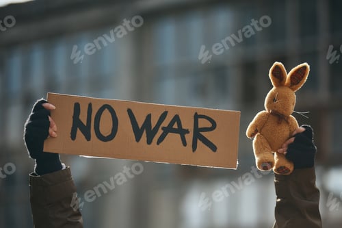 Preview: Close-up of protester with 'no war' placard and plush bunny during anti-war demonstrations.
