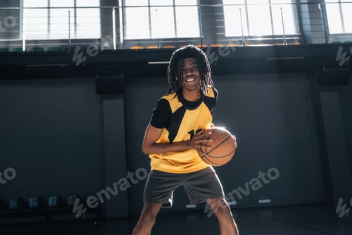 Preview: In yellow sportive clothes. Young black man is playing basketball indoors