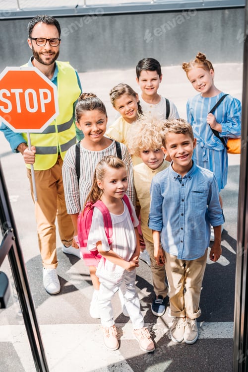 Preview: view from school bus at group of schoolchildren with traffic guard looking at camera