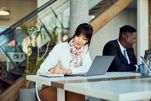 Preview: Focused Woman Taking Notes at a Workplace with Laptop and Coworkers
