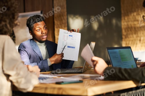 Preview: Young confident broker pointing at document with financial data