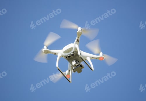 Preview: White drone with digital camera, filming from above. Clear blue sky background.