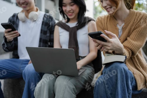 Preview: Group of young asian people using technological devices while studying together outdoors