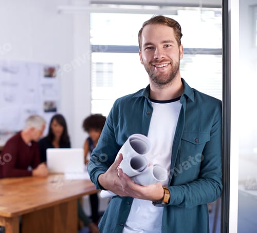 Vista previa: Retrato de un joven arquitecto que sostiene planos con sus colegas trabajando en segundo plano